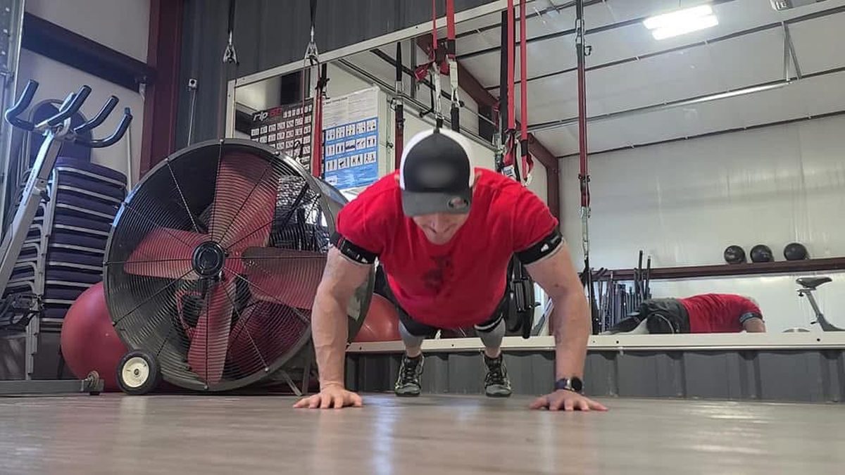 Ty McMillan in a red shirt doing a push-up in a gym, wearing B3 BFR bands