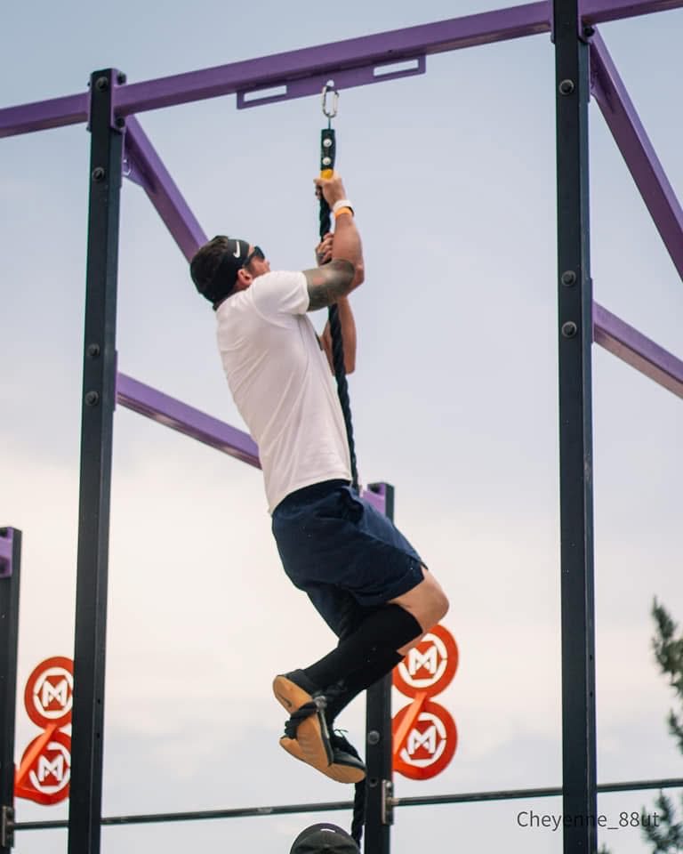 Ty McMillan climbing a rope on an outdoor rig
