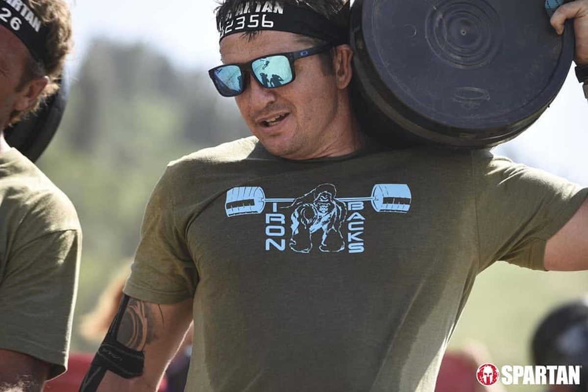 Ty McMillan carrying a weight plate on his shoulder at a Spartan race