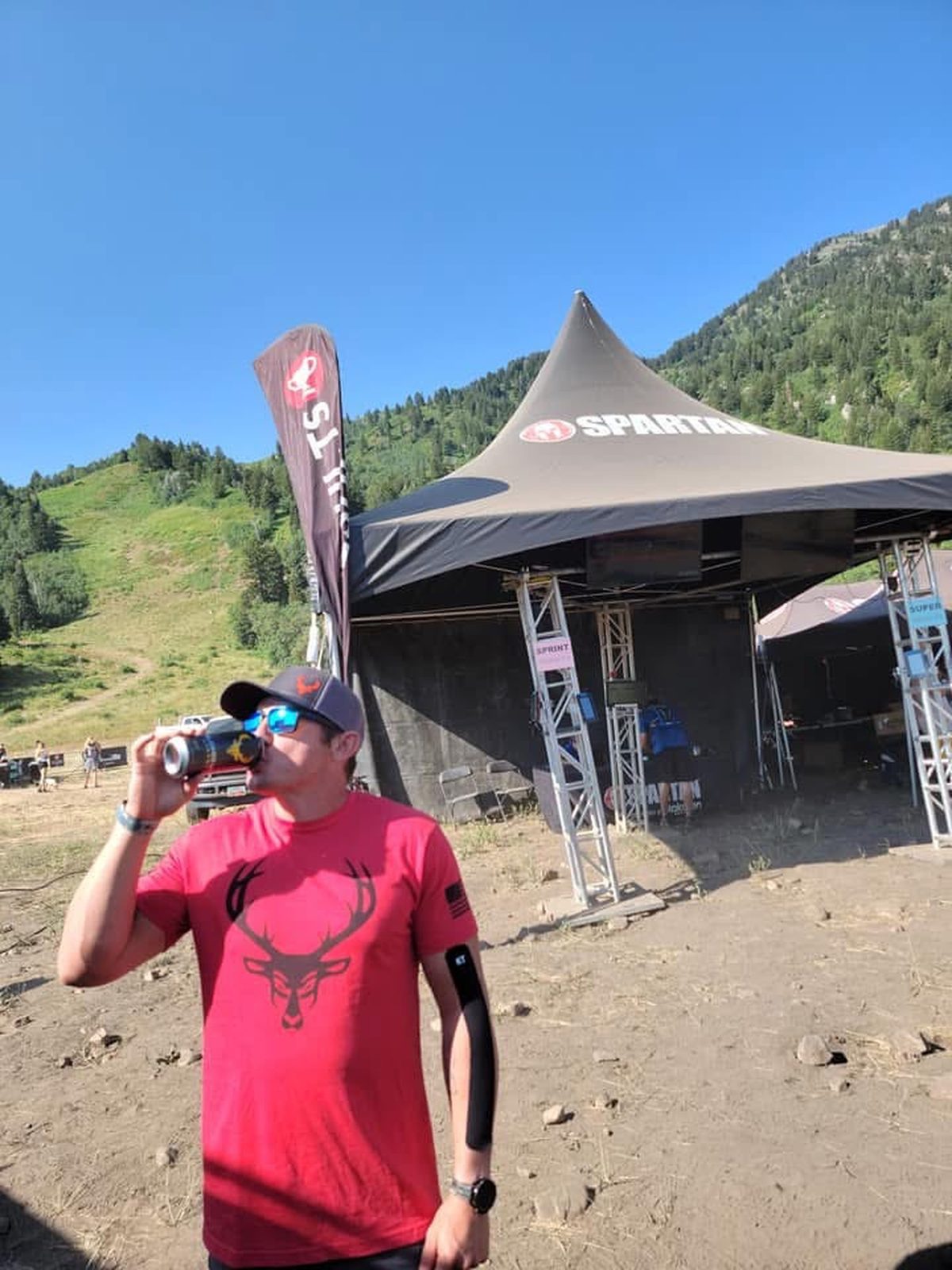 Ty McMillan drinking from a can in front of a Spartan tent in the mountains